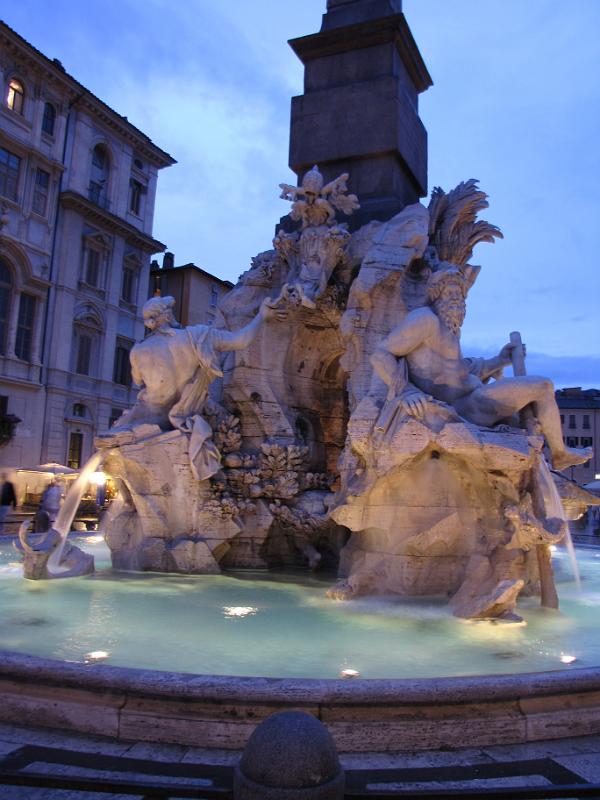 la fontana dei quattro fiumi_bij_avond.jpg - Rond twee uur in de middag is de rondleiding door het Vaticaan afgerond. En we zijn alle vier moe. Moe in de voetjes, maar ook moe in het hoofd na de vele indrukken. Tot de avond gaan we terug naar het apartement.Als de lampjes aangaan, gaan we een ijsje eten en nog even kijken bij een paar mooi verlichtte highlights van Rome.Op de piazza Navona nog een mooie foto van de Vierstromenfontein. Links de riviergod van de Donau die met zijn rechterhand het pauselijk wapenschild ondersteund. Rechts de riviergod van de Ganges die een roeispaan vasthoud om de bevaarbaarheid van de Ganges aan te geven.